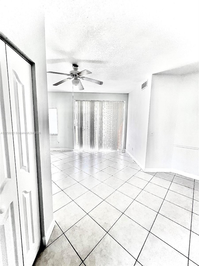 empty room with light tile patterned floors, ceiling fan, a textured ceiling, visible vents, and baseboards