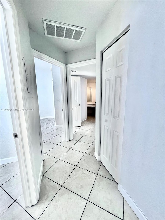 corridor featuring baseboards, visible vents, and light tile patterned flooring