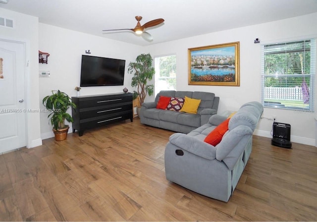 living area featuring baseboards, visible vents, ceiling fan, and wood finished floors