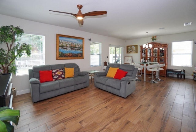 living room with ceiling fan with notable chandelier, light wood finished floors, visible vents, and baseboards