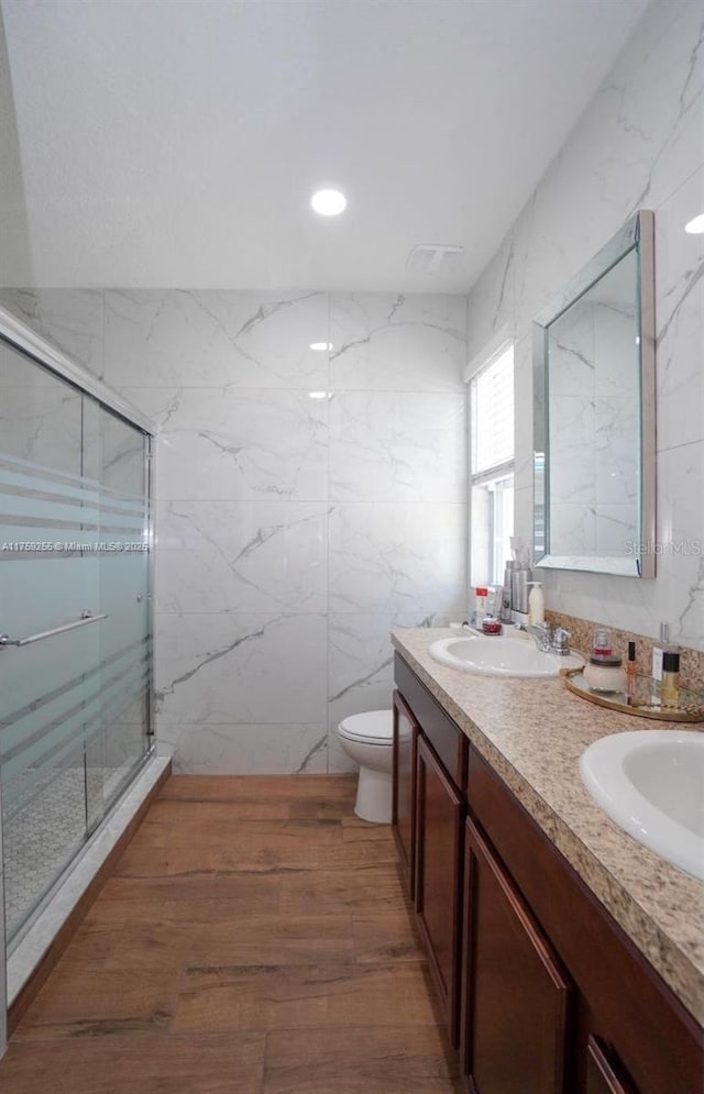 bathroom with double vanity, a marble finish shower, a sink, and wood finished floors