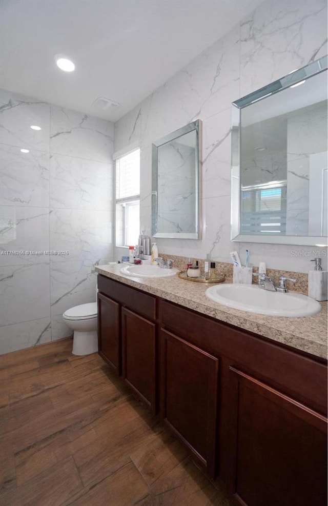 bathroom featuring double vanity, tile walls, toilet, and a sink