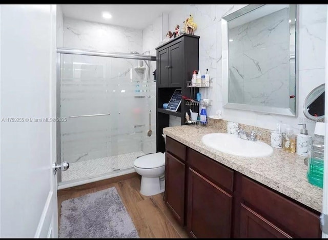 bathroom featuring toilet, wood finished floors, a marble finish shower, and vanity