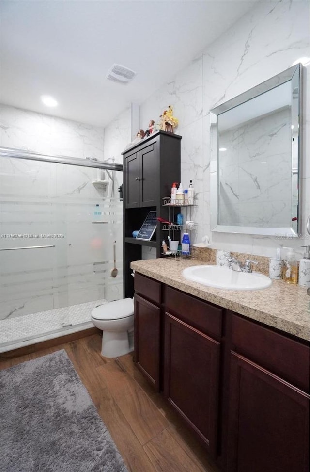 bathroom with toilet, vanity, a marble finish shower, and wood finished floors