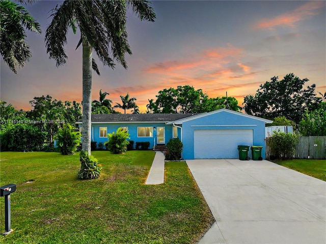 ranch-style home with a garage, fence, a yard, driveway, and stucco siding