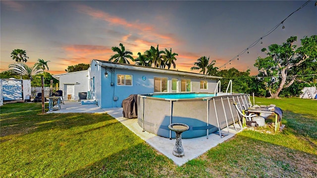 back of house at dusk with a fenced in pool, a patio, a lawn, and stucco siding