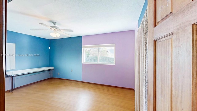 unfurnished room featuring a textured ceiling, wood finished floors, a ceiling fan, and baseboards