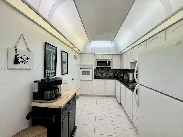 kitchen with marble finish floor, tasteful backsplash, white appliances, butcher block counters, and vaulted ceiling