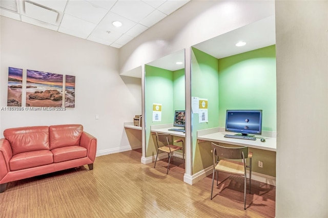 office area featuring a paneled ceiling, baseboards, wood finished floors, and built in desk