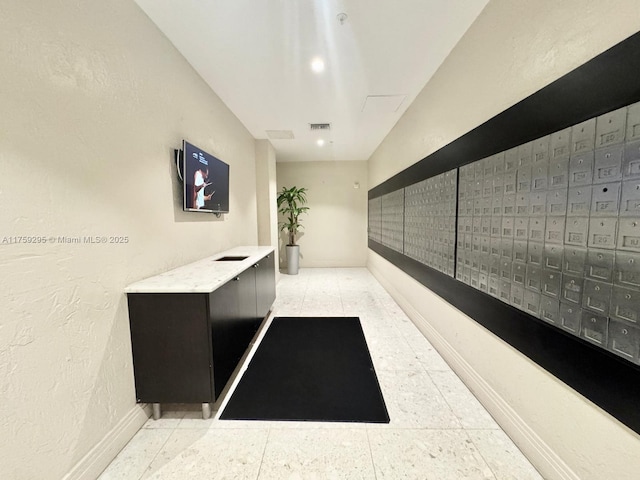 corridor featuring mail area, baseboards, and a textured wall