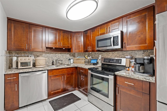 kitchen with stainless steel appliances, backsplash, a sink, and light stone countertops