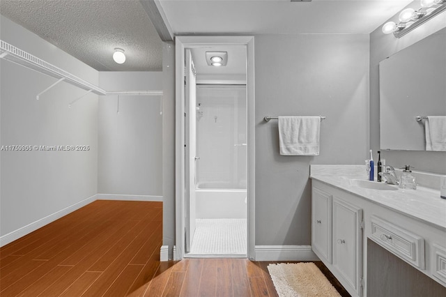 bathroom featuring a spacious closet, a textured ceiling, vanity, wood finished floors, and baseboards