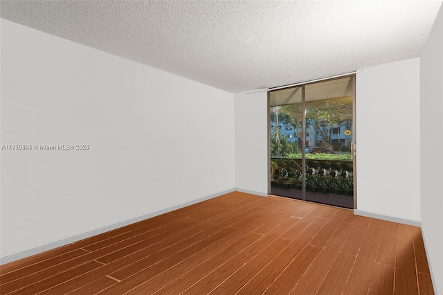 empty room with floor to ceiling windows, a textured ceiling, baseboards, and wood finished floors