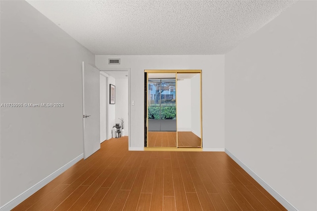 empty room with visible vents, a textured ceiling, baseboards, and wood finished floors