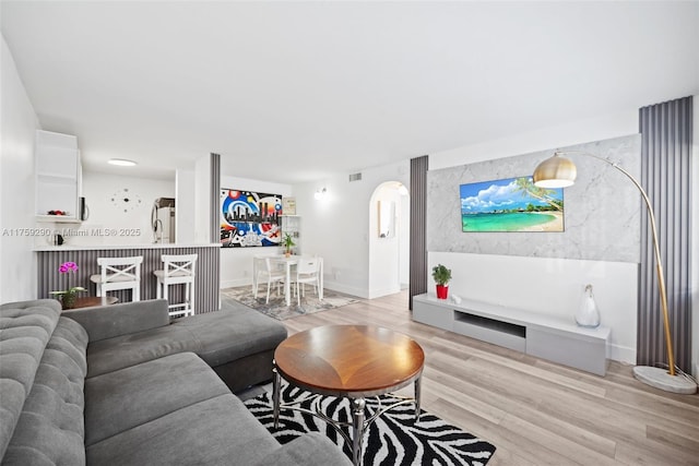living room featuring arched walkways, light wood-style floors, baseboards, and an accent wall