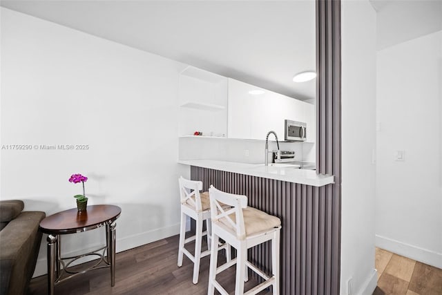 kitchen with white cabinetry, a kitchen bar, stainless steel microwave, and wood finished floors