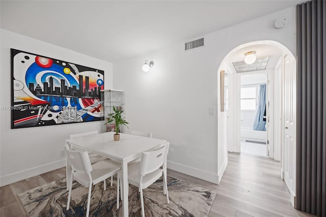 dining room featuring arched walkways, baseboards, visible vents, and light wood-style floors