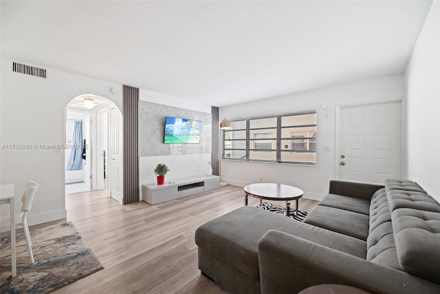 living room featuring arched walkways, wood finished floors, visible vents, and baseboards