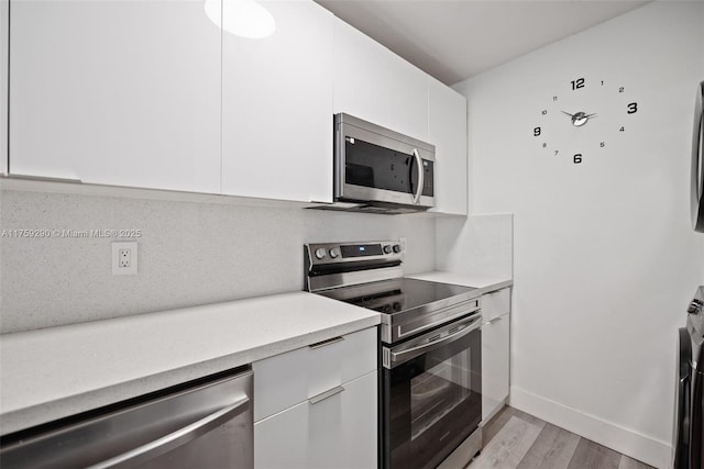 kitchen featuring light wood-style flooring, white cabinets, light countertops, appliances with stainless steel finishes, and decorative backsplash