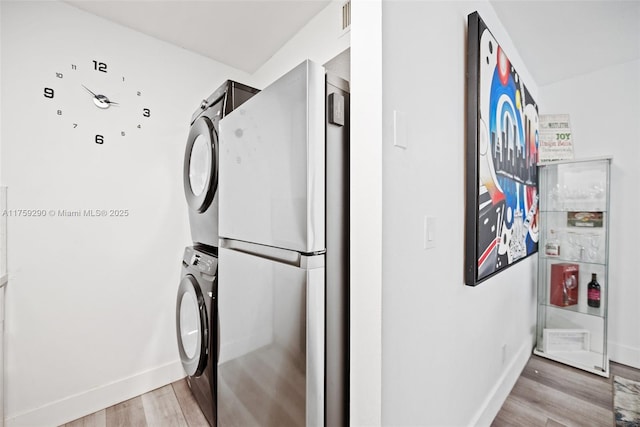 clothes washing area with stacked washer / dryer, light wood finished floors, and baseboards