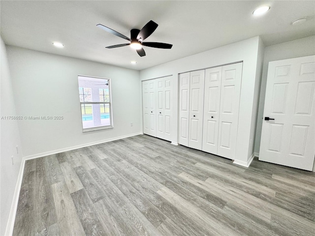 unfurnished bedroom featuring baseboards, a ceiling fan, wood finished floors, two closets, and recessed lighting