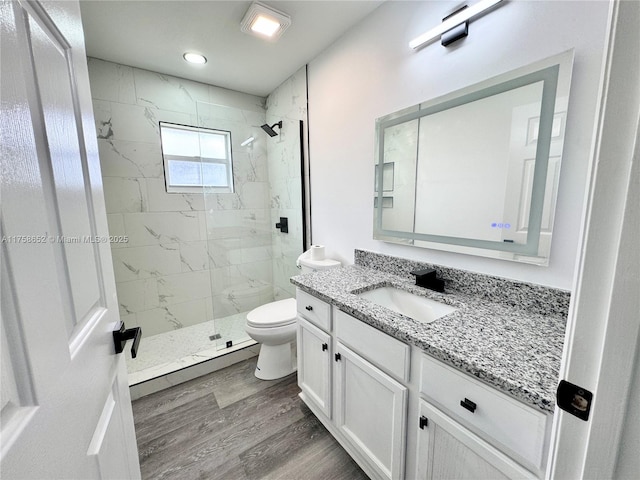 full bathroom featuring toilet, a marble finish shower, wood finished floors, and vanity