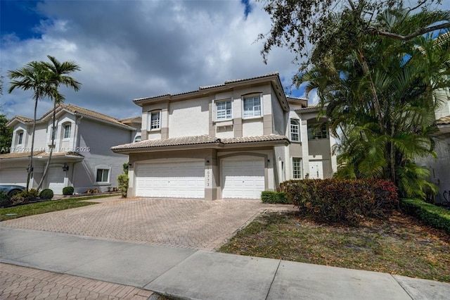 mediterranean / spanish house featuring a garage, decorative driveway, a tile roof, and stucco siding