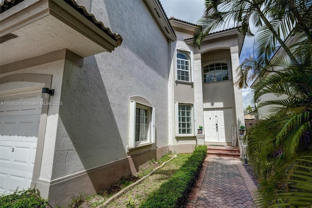 doorway to property featuring a garage, a tiled roof, and stucco siding