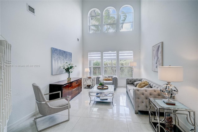 tiled living area featuring baseboards, a high ceiling, visible vents, and a healthy amount of sunlight