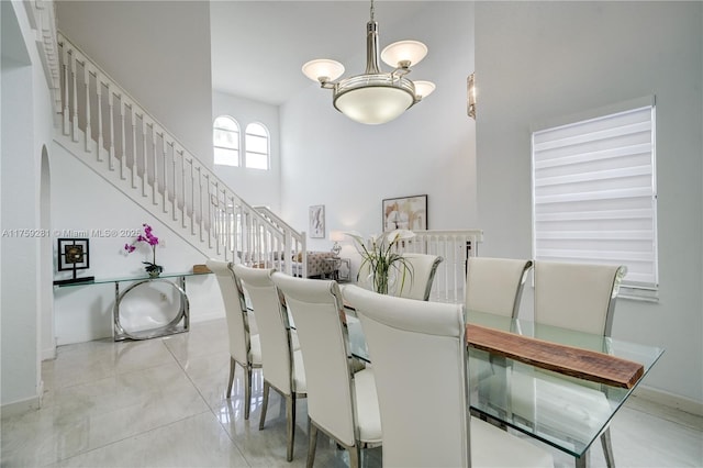 dining area with tile patterned flooring, a notable chandelier, a high ceiling, baseboards, and stairs