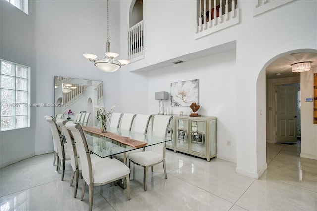 dining area featuring baseboards, visible vents, arched walkways, a towering ceiling, and an inviting chandelier