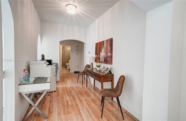 corridor featuring arched walkways, light wood-type flooring, and baseboards