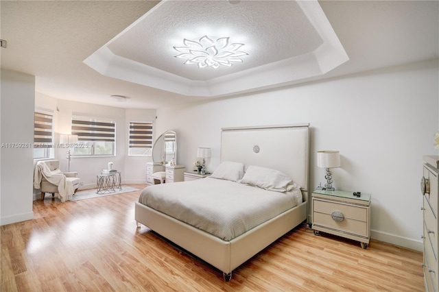 bedroom featuring light wood-style floors, a raised ceiling, a textured ceiling, and baseboards