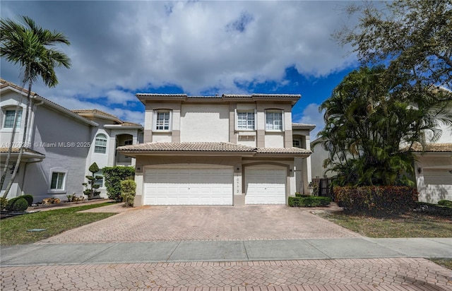 mediterranean / spanish home featuring decorative driveway, an attached garage, a tile roof, and stucco siding