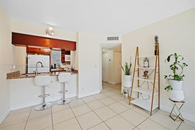 kitchen with visible vents, stone countertops, tile patterned flooring, white appliances, and a kitchen bar