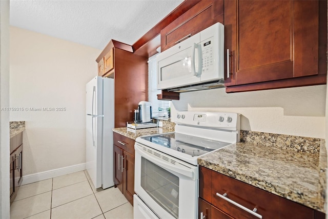 kitchen with light stone counters, light tile patterned floors, a textured ceiling, white appliances, and baseboards