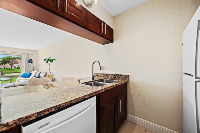 kitchen with stone countertops, light tile patterned flooring, a sink, white appliances, and baseboards