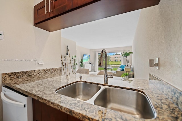 kitchen featuring a textured wall, dishwashing machine, light stone counters, and a sink