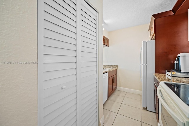 kitchen featuring range with electric cooktop, light stone counters, freestanding refrigerator, a textured ceiling, and light tile patterned flooring