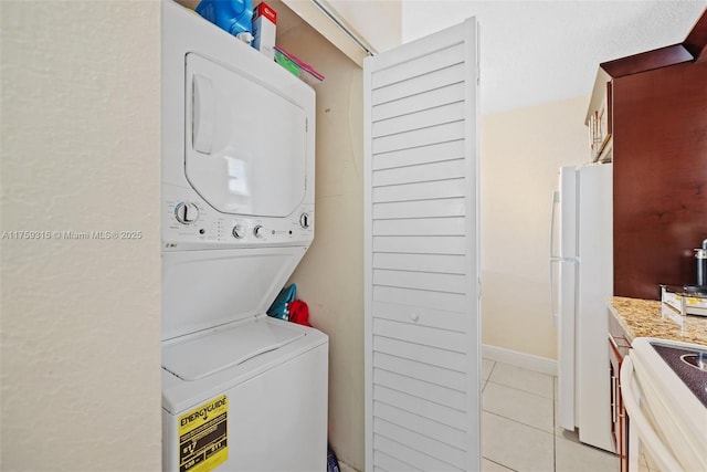 laundry room with laundry area, baseboards, stacked washer / drying machine, and light tile patterned flooring