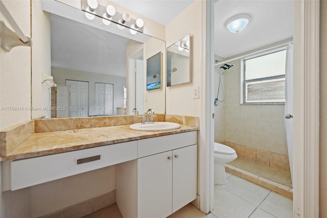 bathroom with toilet, tile patterned flooring, tiled shower, and vanity