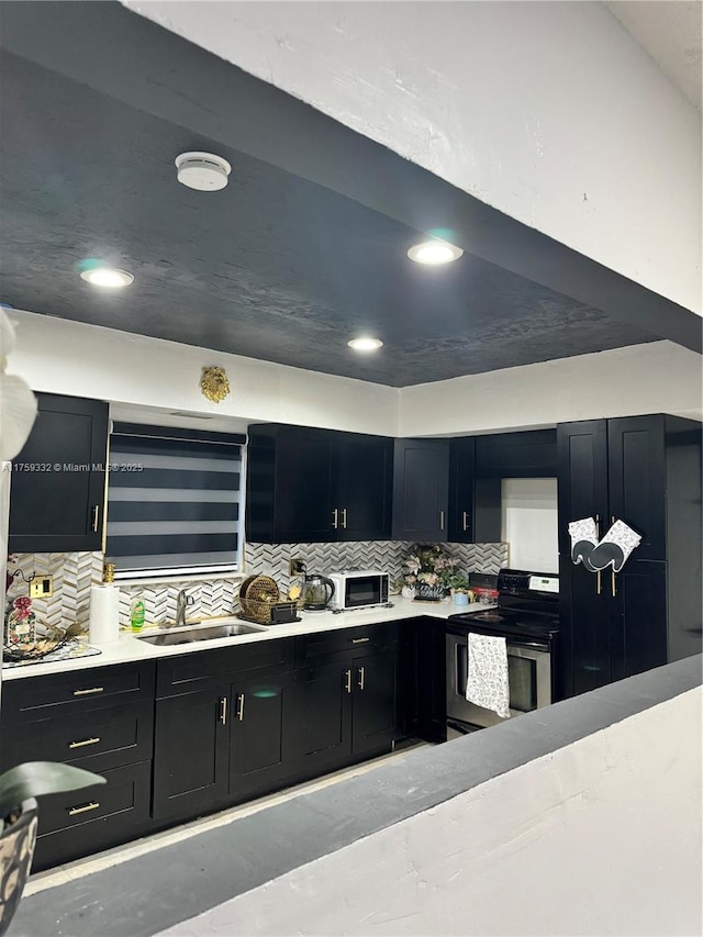 kitchen featuring dark cabinetry, stainless steel electric stove, light countertops, and a sink