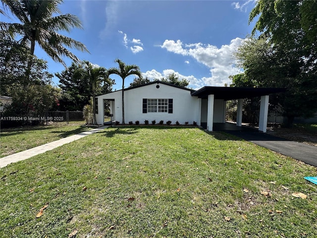 view of front facade with stucco siding, a front yard, fence, a carport, and driveway