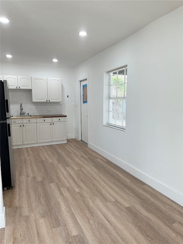 kitchen featuring light wood finished floors, tasteful backsplash, white cabinetry, fridge with ice dispenser, and a sink