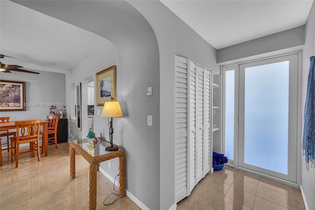 foyer entrance featuring arched walkways, light tile patterned floors, baseboards, and ceiling fan