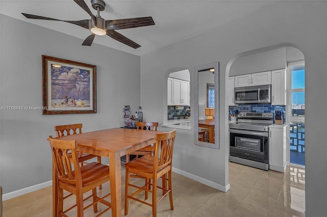 dining area with baseboards, arched walkways, light tile patterned flooring, and a ceiling fan