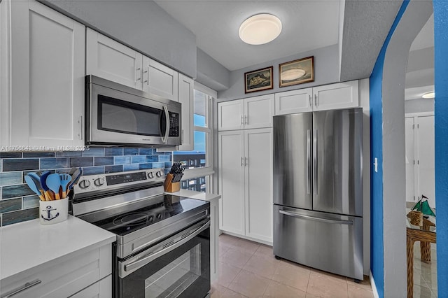 kitchen with arched walkways, stainless steel appliances, decorative backsplash, light countertops, and white cabinetry