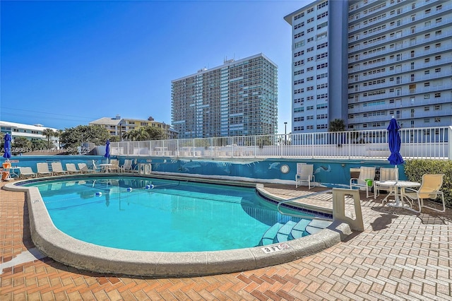 community pool with a patio area, a view of city, and fence