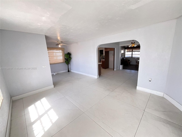 empty room featuring arched walkways, ceiling fan, a textured ceiling, and baseboards