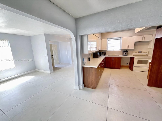 kitchen featuring white electric range oven, baseboards, arched walkways, white cabinets, and light countertops